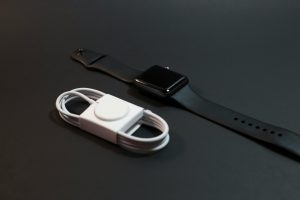 Close-up of a black smartwatch and white charging cable on a dark surface. Ideal for technology themes.