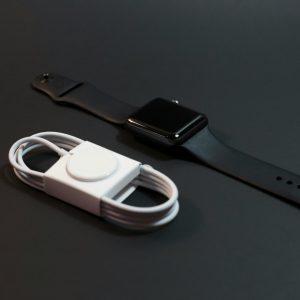 Close-up of a black smartwatch and white charging cable on a dark surface. Ideal for technology themes.